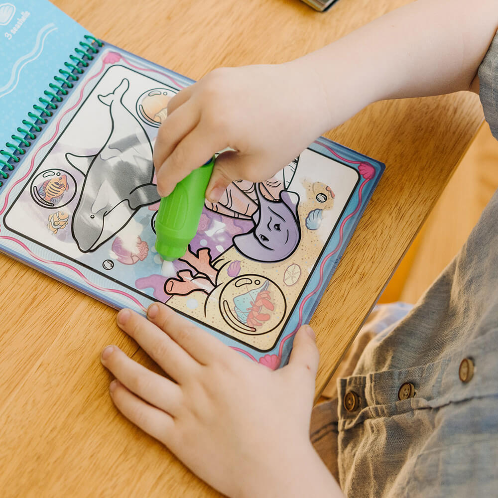 Child's hands shown with the pen full of water coloring the page of the Melissa and Doug Water Wow! Animals Water-Reveal On the Go Travel Activity Pad